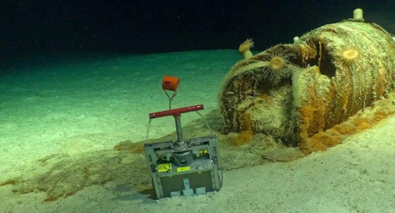 Un des fûts de déchets radioactifs présentant une dégradation importante et un déversement de matière sur les fonds marins environnants. On voit, à côté, le dispositif d’échantillonnage des sédiments déployé puis récupéré par le Nautile à 4 700 mètres de profondeur, en 2026. Crédits: Campagne NODSSUM, CNRS, Flotte océanographique française, Ifremer, Miso Facility/WHOI, Fourni par l'auteur